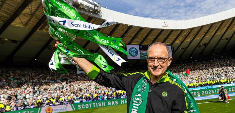 Man holding trophy with Celtic fans in background