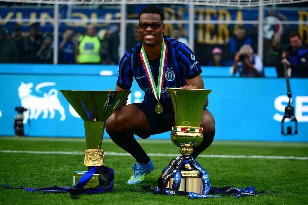 Player celebrating with two trophies on the pitch