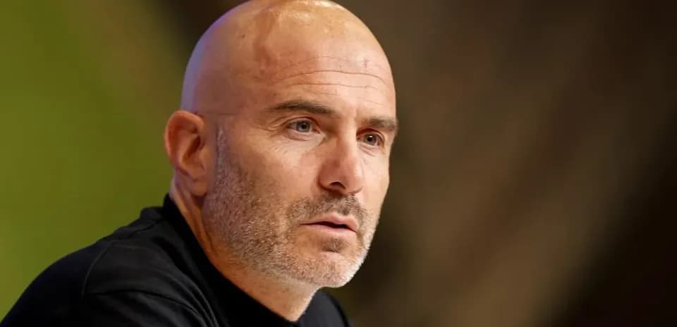 Coach speaking at press conference with serious expression