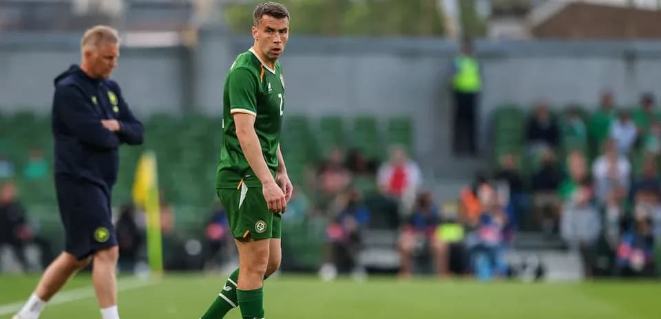 Player in green kit during match, coach in background