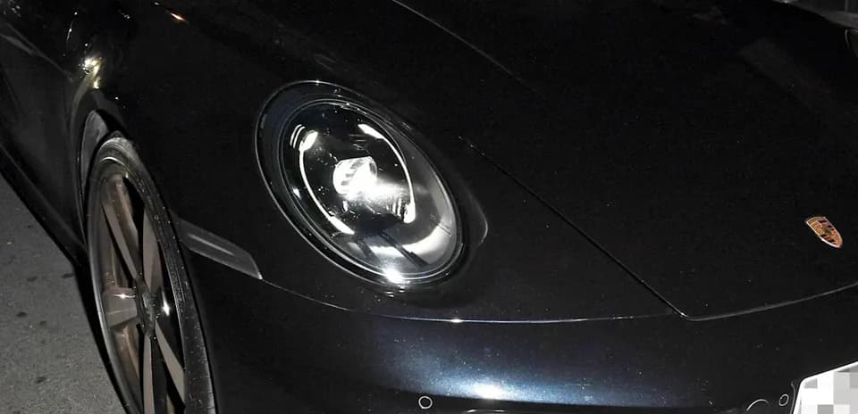 Two men sitting in a black Porsche sports car
