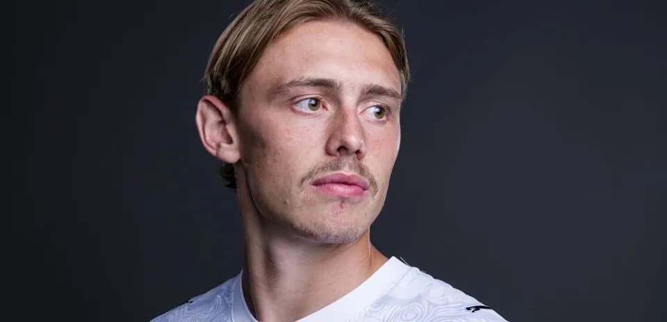 Player posing in white jersey against dark background