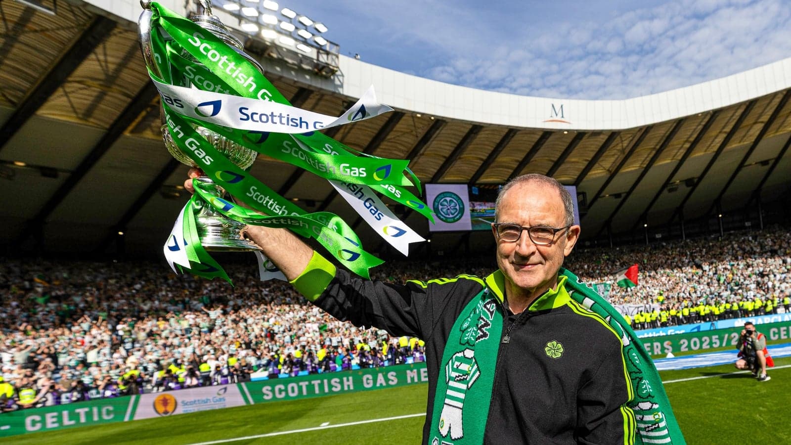 Man holding trophy with Celtic fans in background Man holding trophy with Celtic fans in background