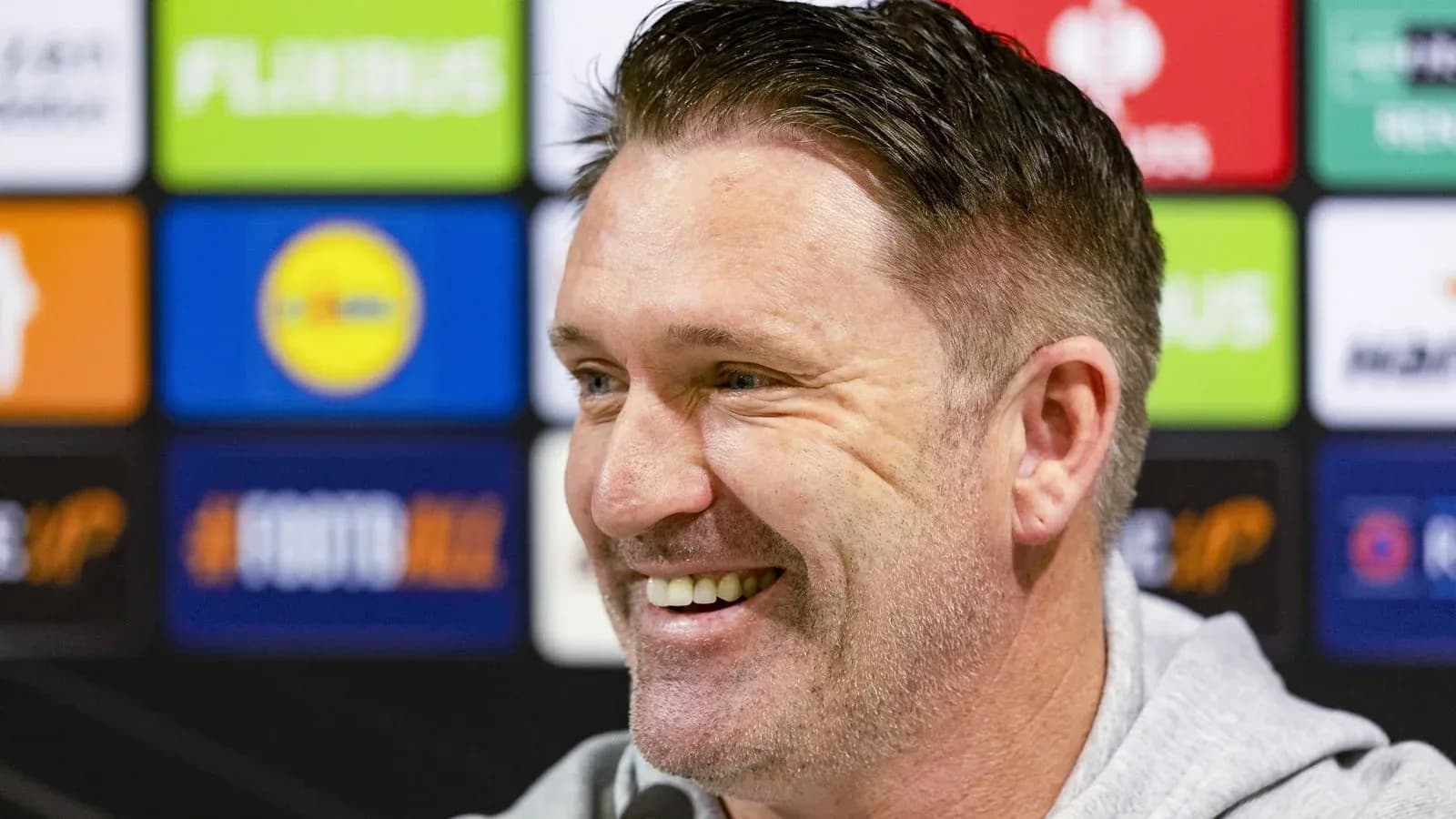 Coach smiling during press conference with logos behind Coach smiling during press conference with logos behind