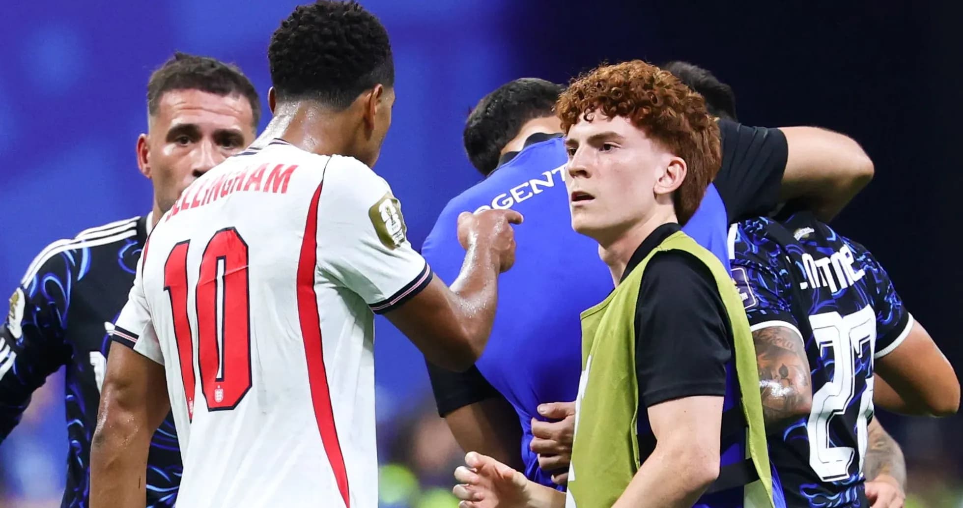 Players interacting during a match, with substitutes nearby Players interacting during a match, with substitutes nearby