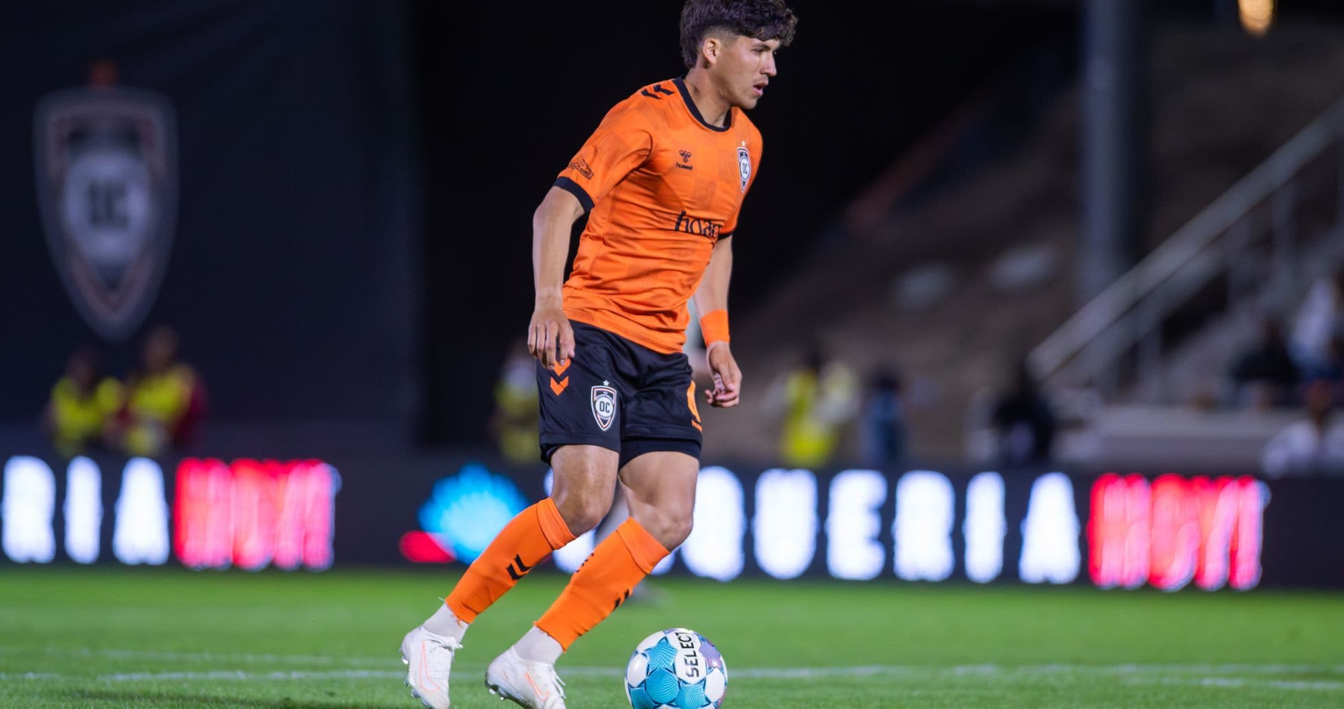 Player in orange kit dribbling ball on field Player in orange kit dribbling ball on field